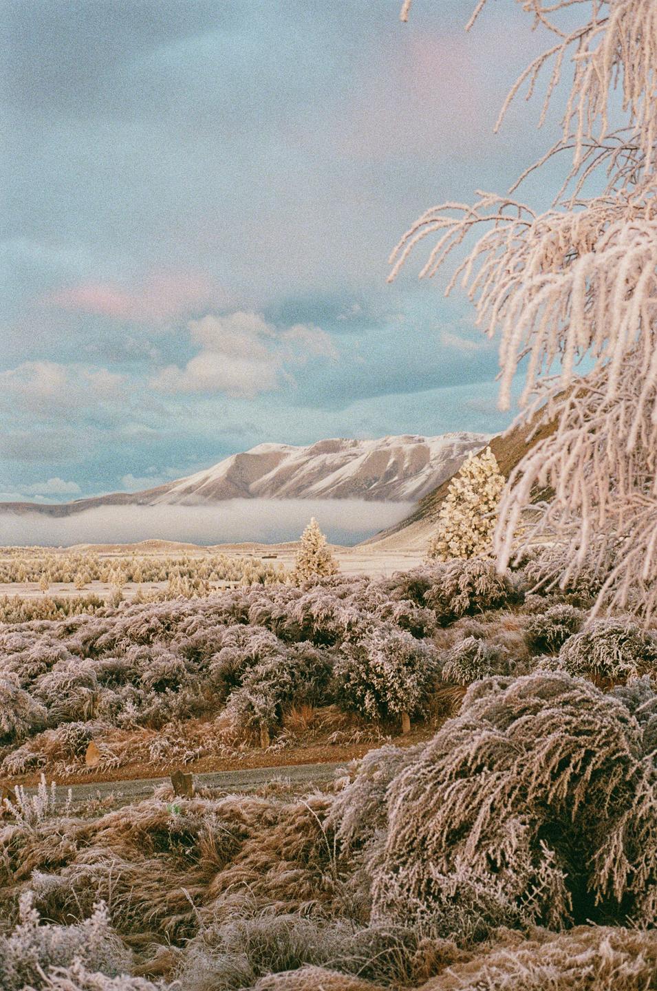 A frosty landscape with snow-capped mountains and a cloudy sky.