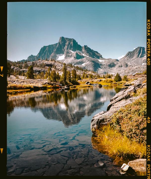 A clear mountain lake reflects a snow-capped peak under a bright sky.