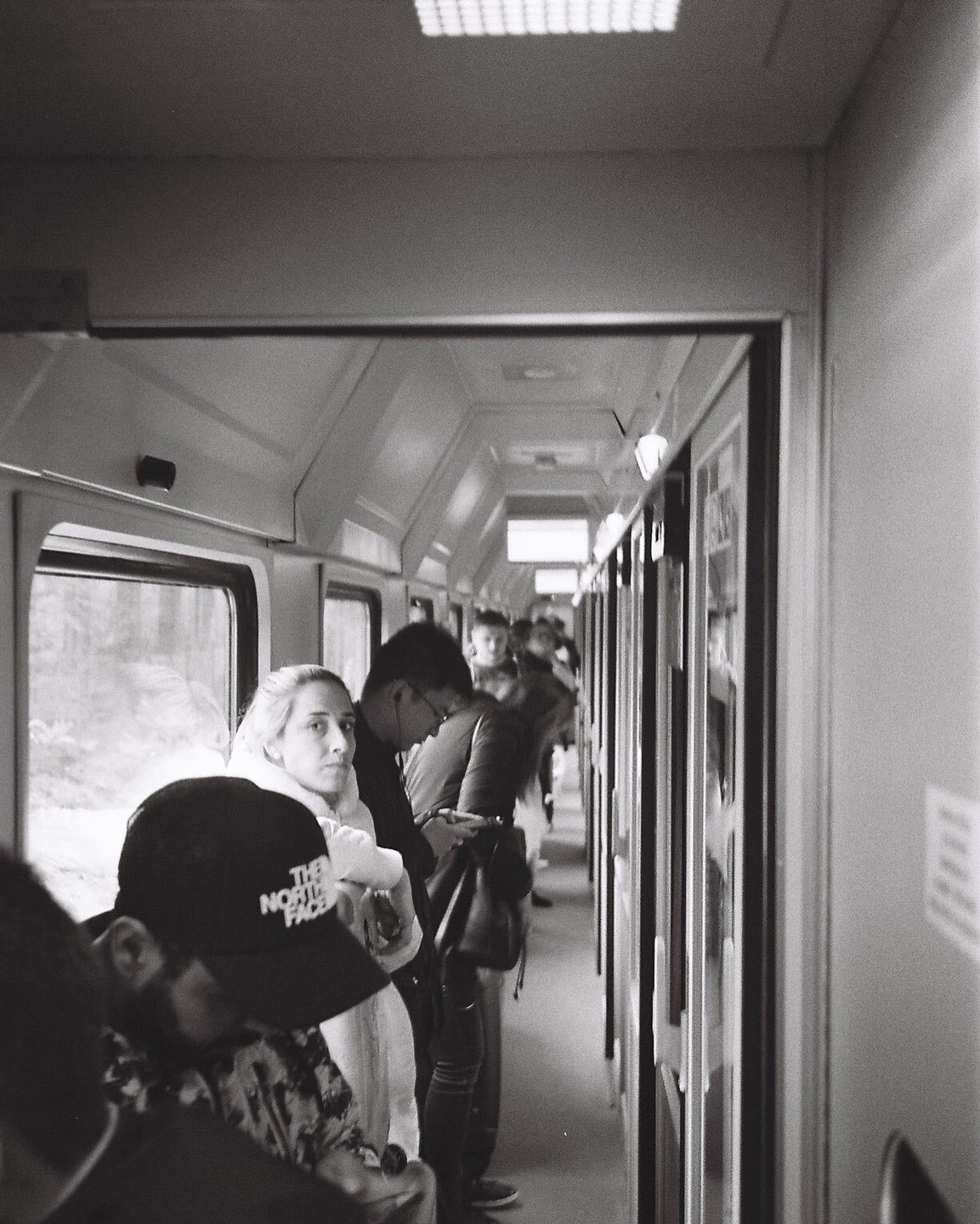 People stand in the narrow aisle of a train car.