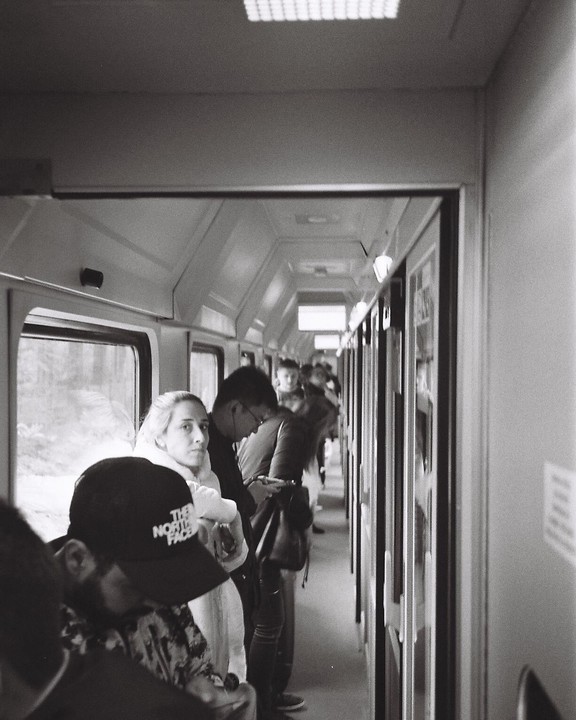 People stand in the narrow aisle of a train car.