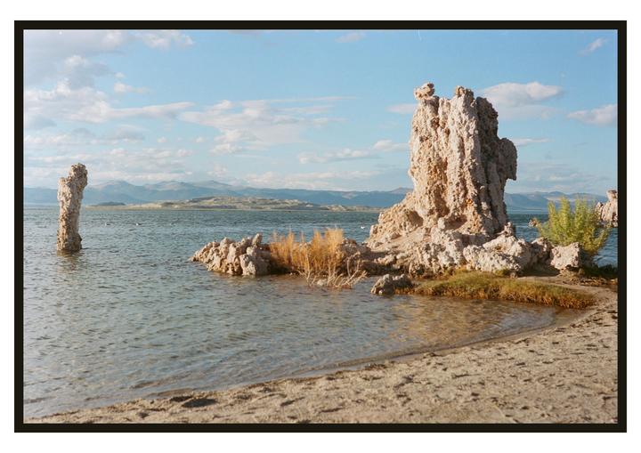 Tufa formations rise from the water and line the shore of Mono Lake under a partly cloudy sky.