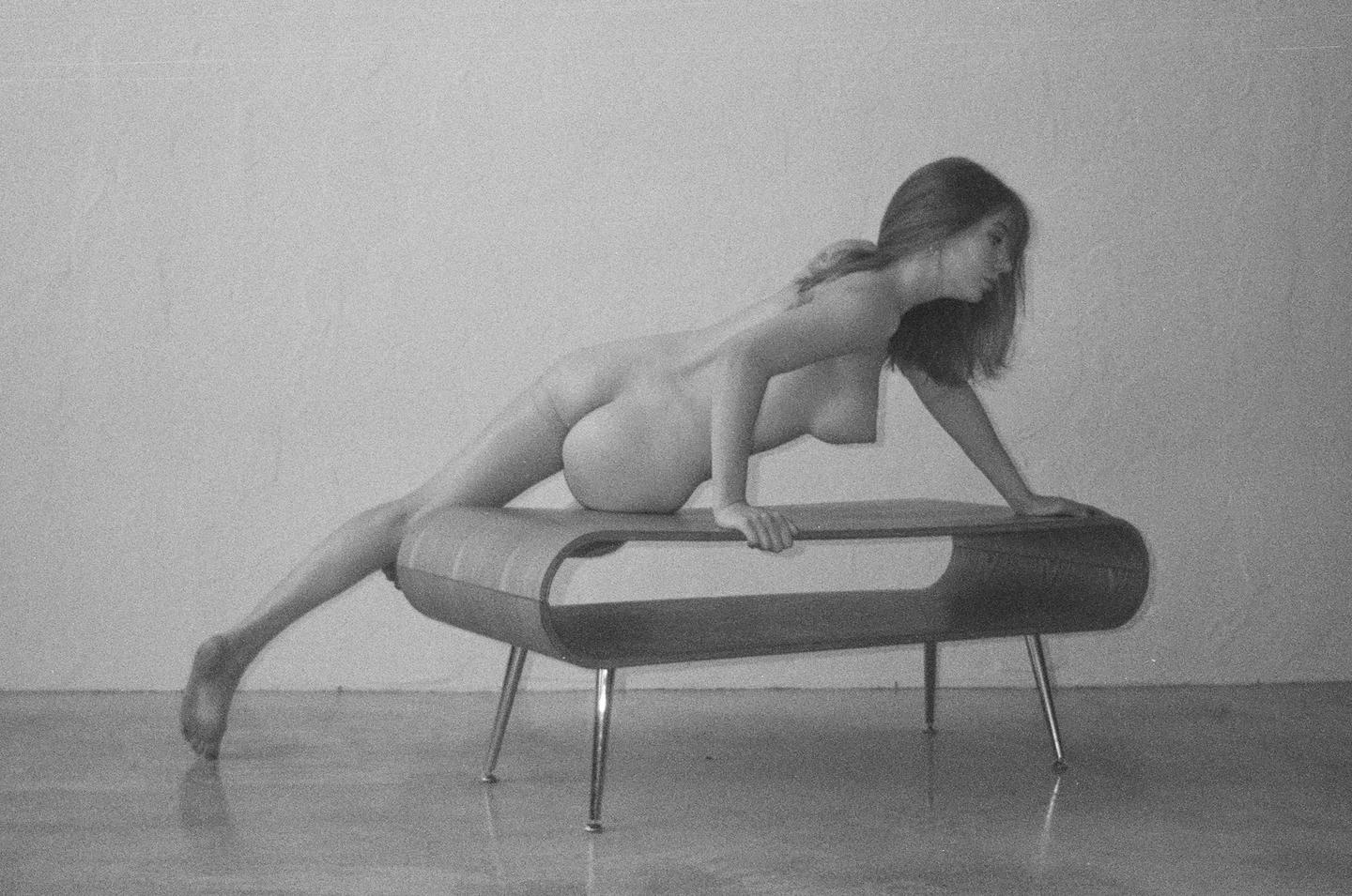A nude woman is posed on a low bench.