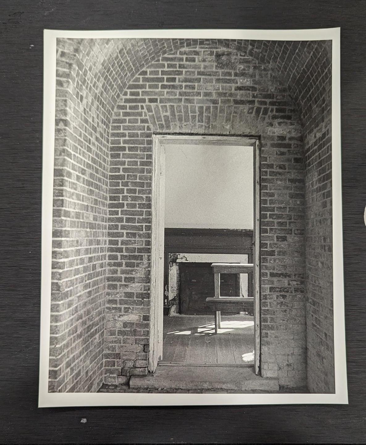 A brick archway leads to a room with a wooden floor and a table.