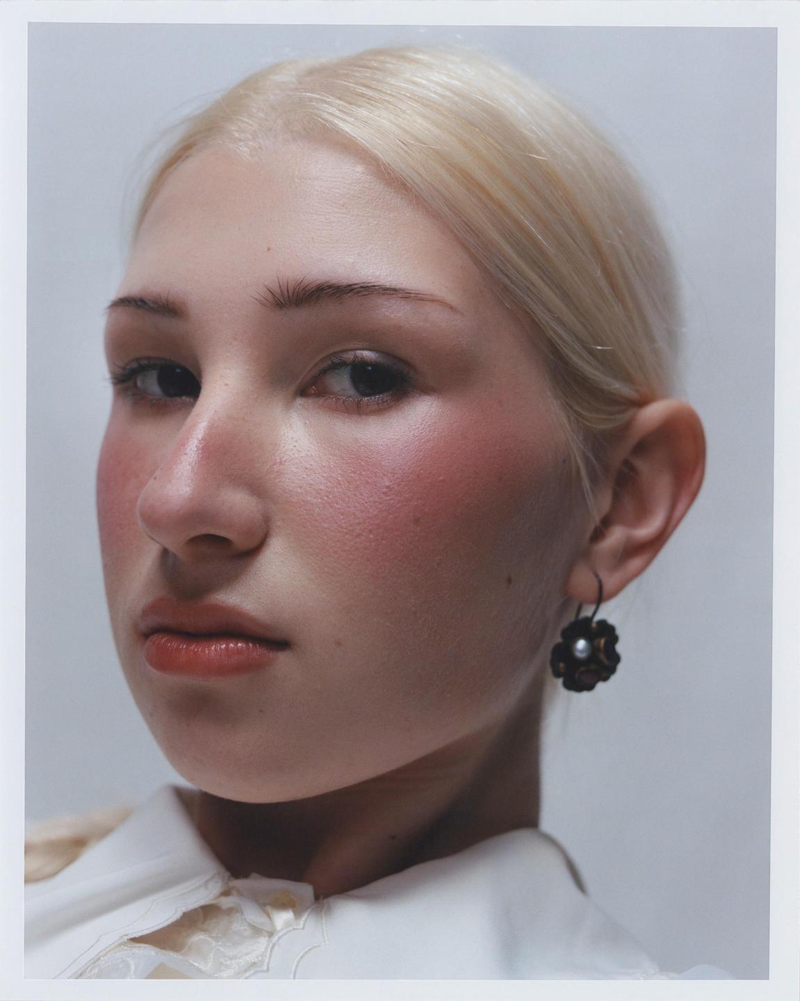 A woman with blonde hair and rosy cheeks looks directly at the viewer.