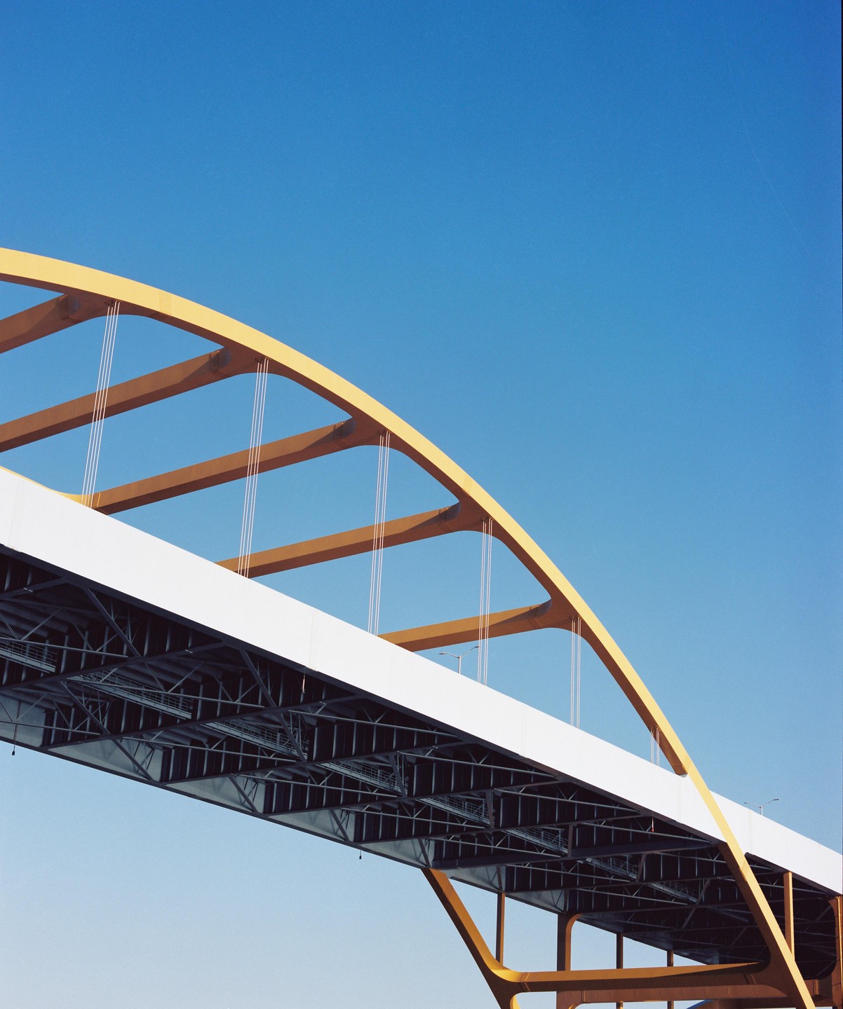 A yellow and white bridge with a clear blue sky in the background is shown from below.