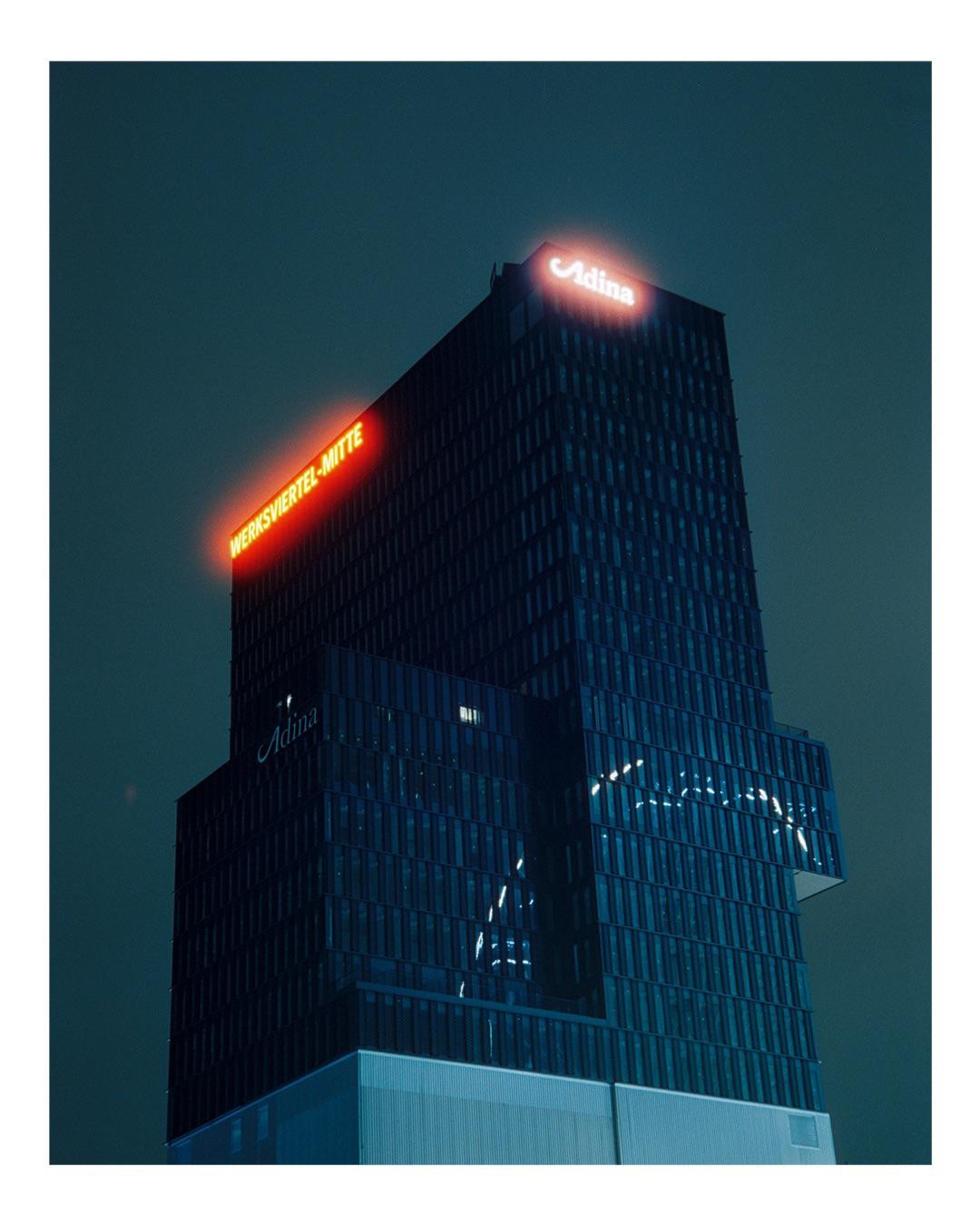 A tall, dark building with glowing red and white signs stands against a dark sky at night.