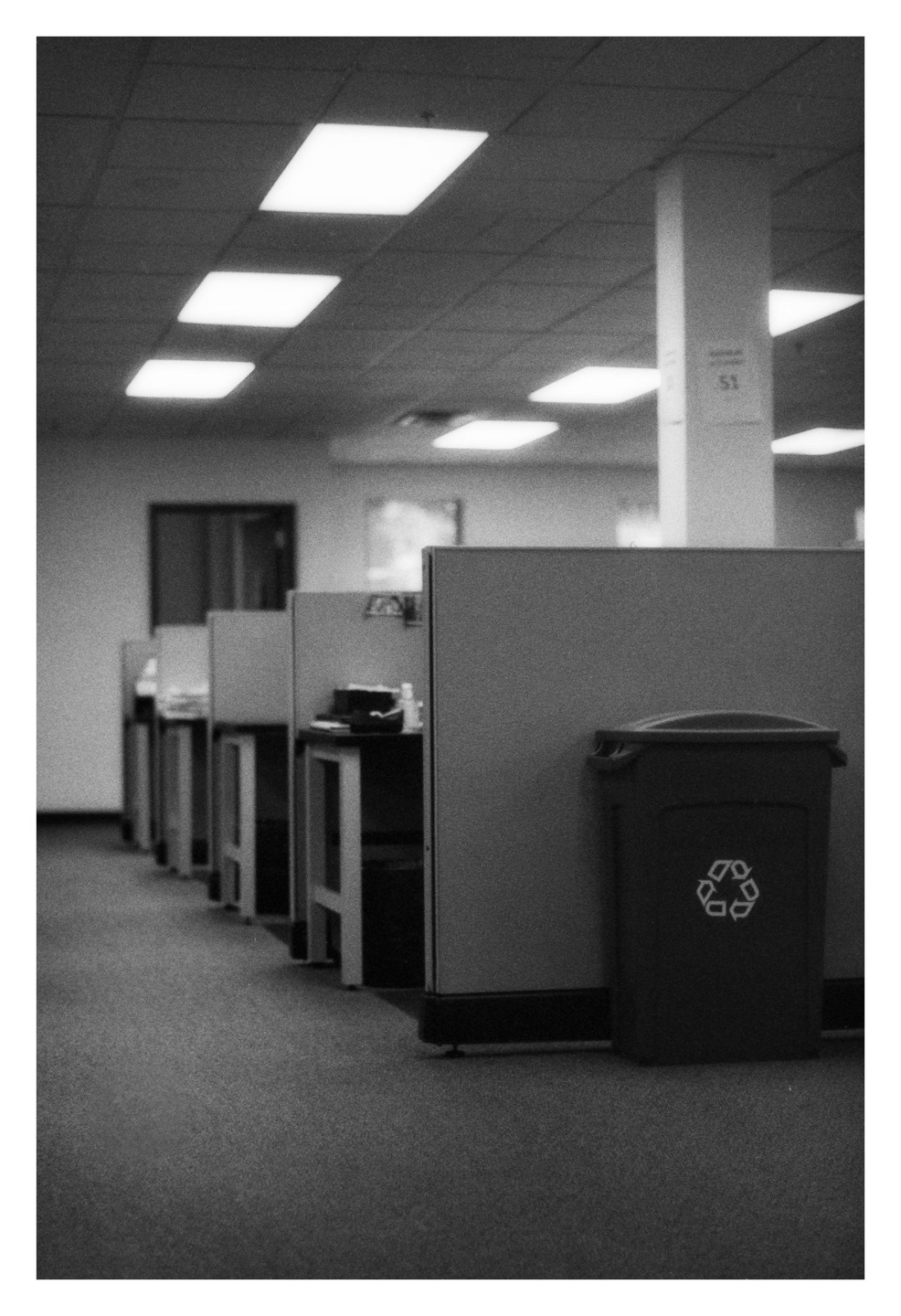 A row of empty office cubicles with a recycling bin in the foreground.
