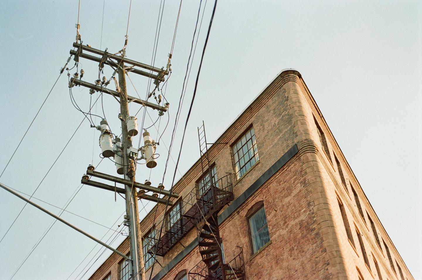 A low-angle view shows a utility pole with many wires and a brick building with a spiral fire escape.