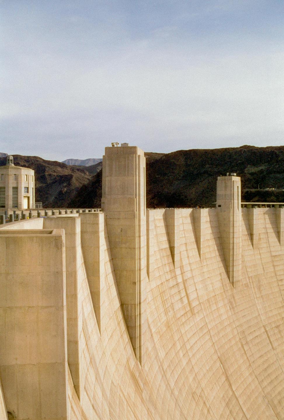 The Hoover Dam is visible with mountains in the background under a cloudy sky.