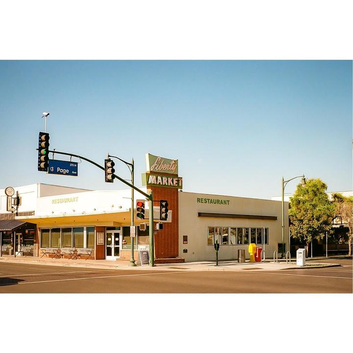 A restaurant and market building stands on a street corner with traffic lights and a clear sky above.