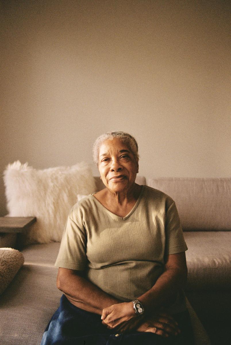 A woman sits on a sofa with her hands clasped in her lap.