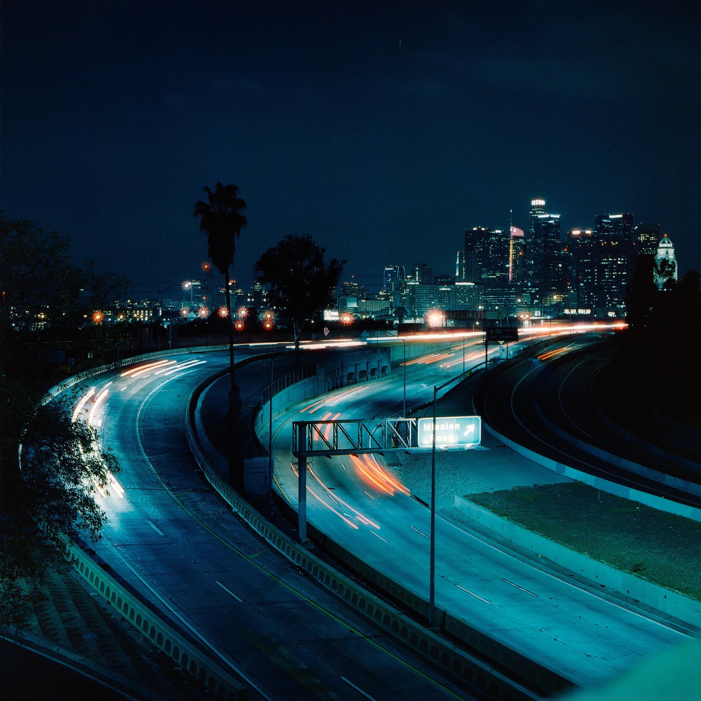 A highway with light trails from vehicles curves towards a city skyline at night.