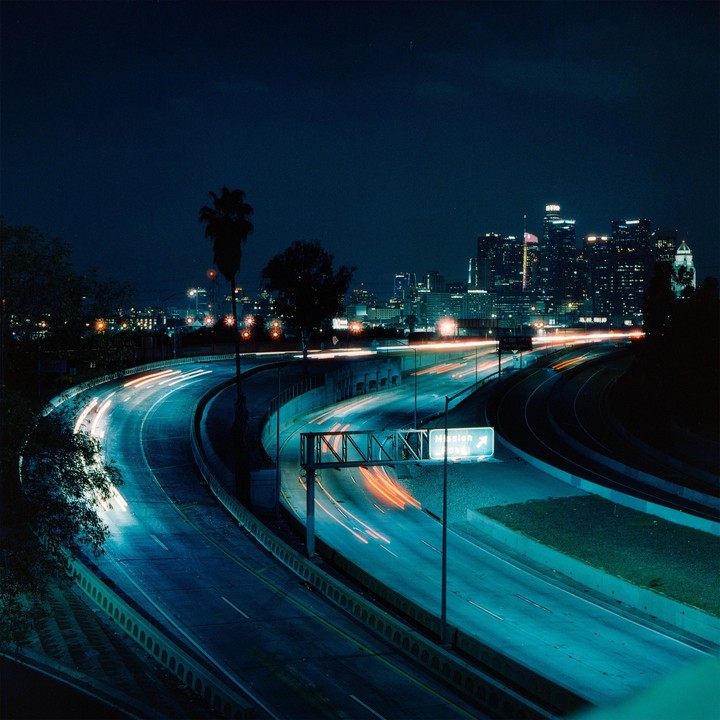 A highway with light trails from vehicles curves towards a city skyline at night.