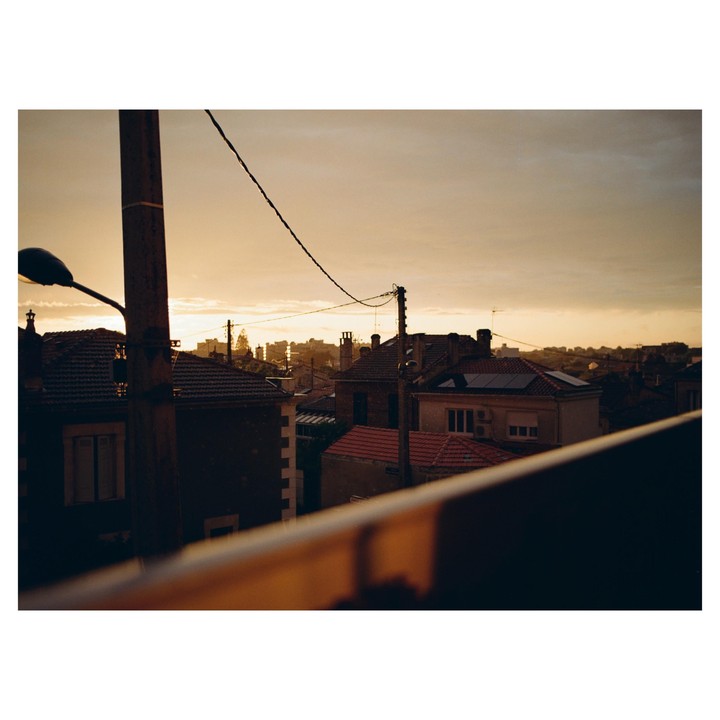 The last light of sunset illuminates a town with houses and power lines.