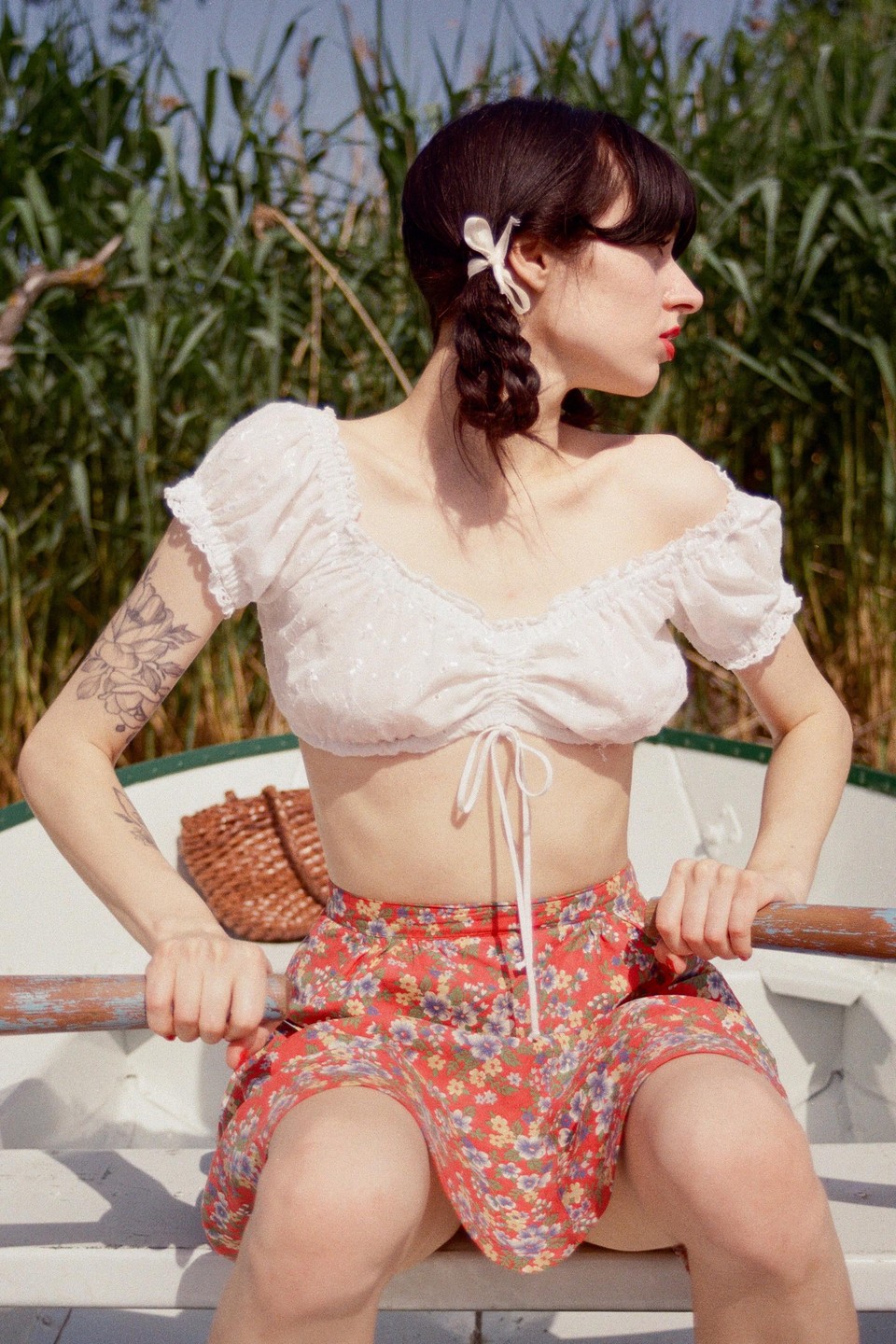 A woman with braided hair and a floral skirt sits in a boat, holding an oar.