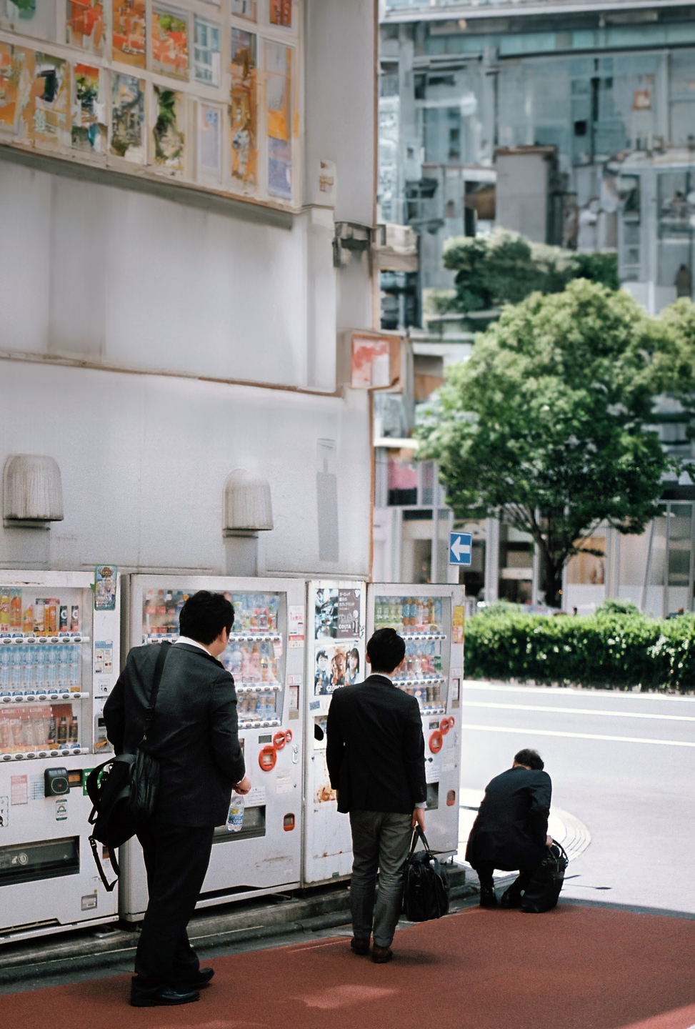 Three men in suits stand near vending machines on a city street.