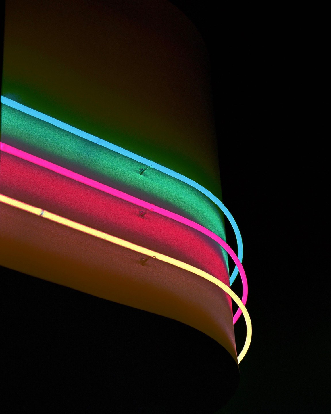 Three neon lights in blue, pink, and yellow curve around a dark surface.