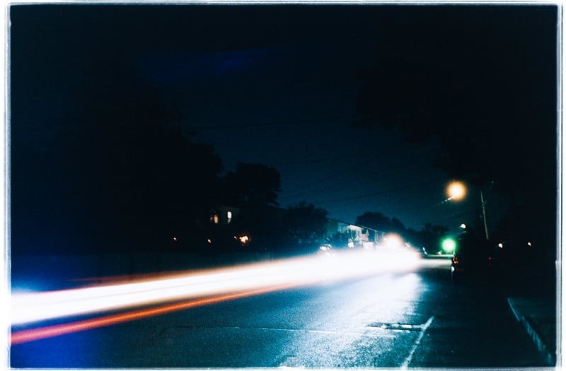 Headlights and taillights create light trails on a wet street at night.