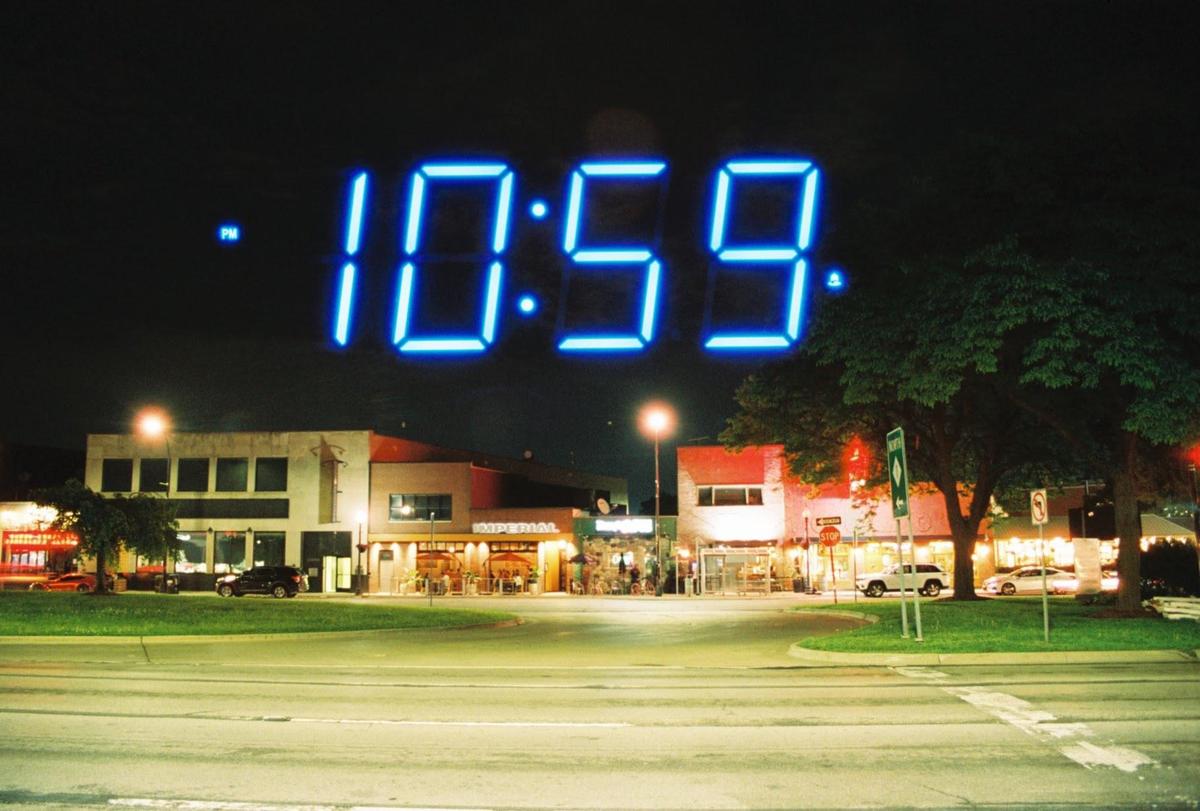 A large blue digital clock displaying 10:59 is superimposed over a street scene with buildings and trees at night.