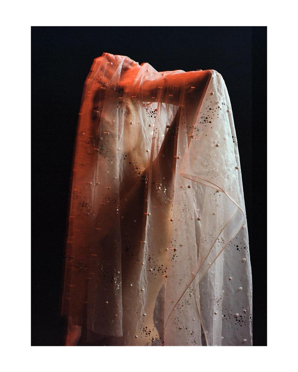 A person is visible behind a translucent, beaded fabric.