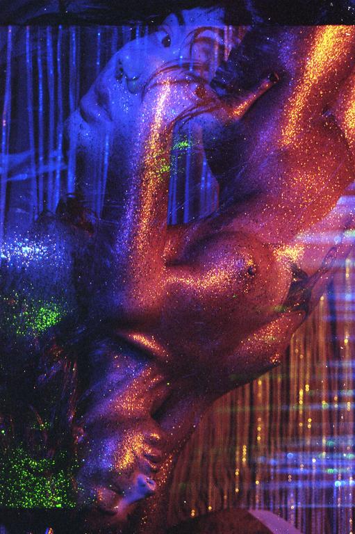 A woman's body is covered in glitter and illuminated by neon light in a double exposure.