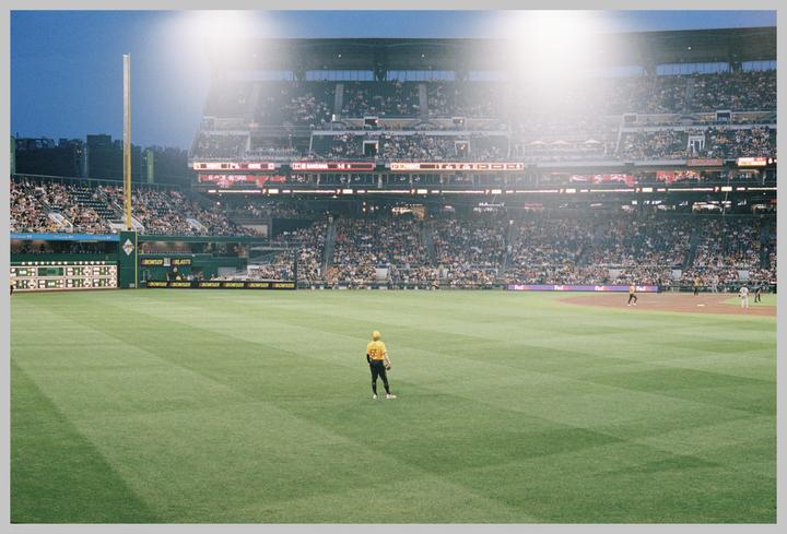 A baseball player stands on a green field in a stadium filled with spectators under bright lights.