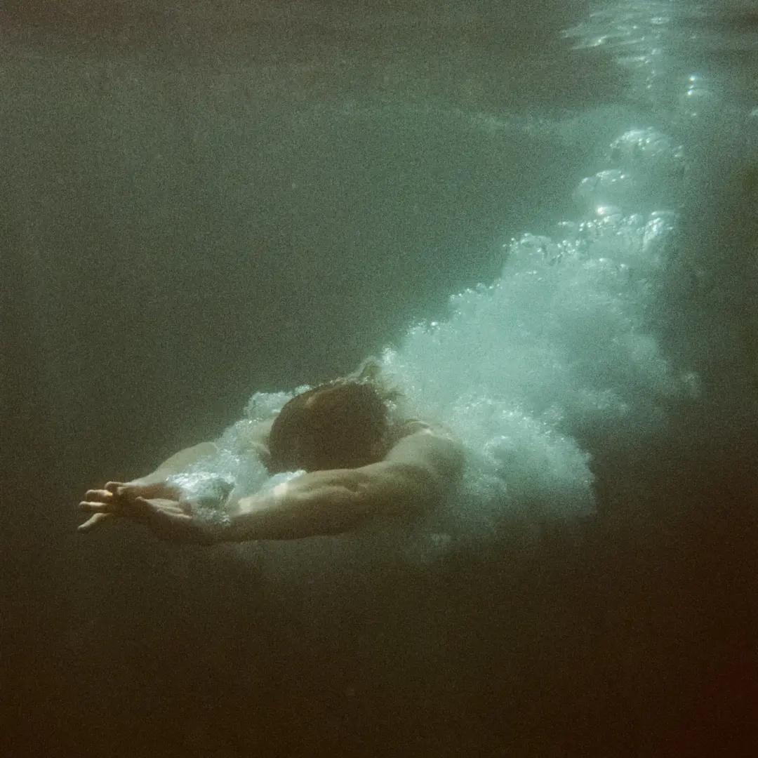 A man dives into dark water, creating a trail of bubbles behind him.