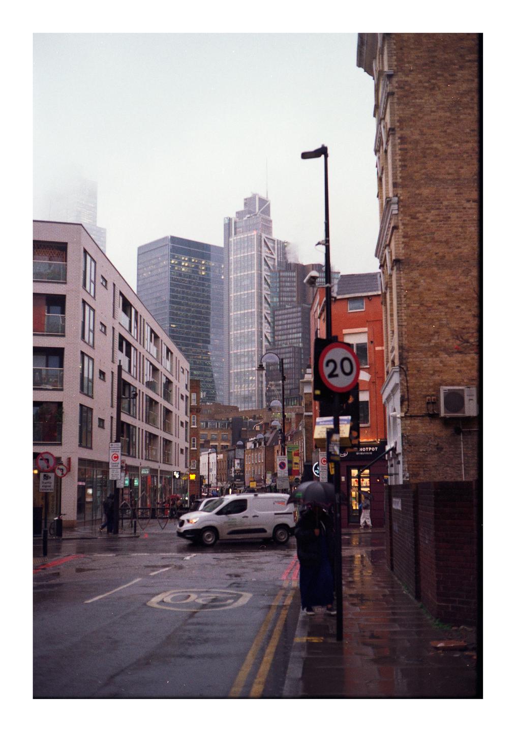 A street scene shows a white van driving on a wet road with tall buildings in the background.