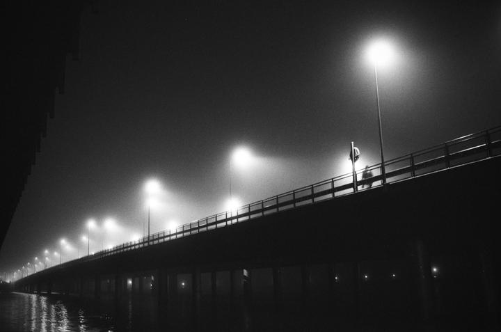 A person walks on a bridge illuminated by streetlights at night.