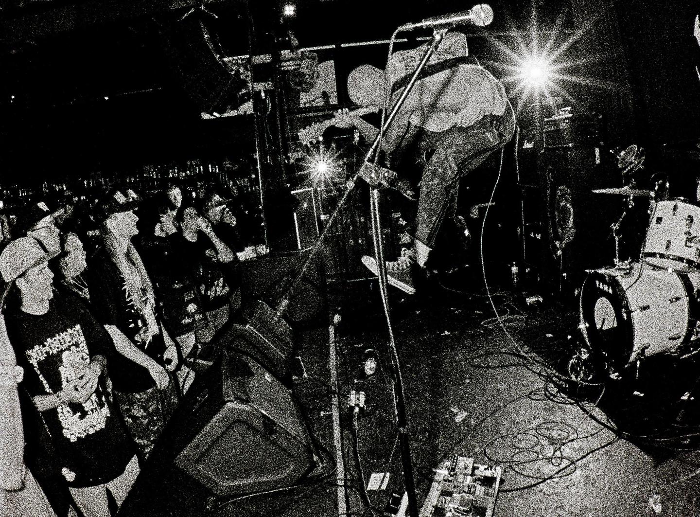 A musician plays guitar on stage in front of a crowd at a hardcore music concert.