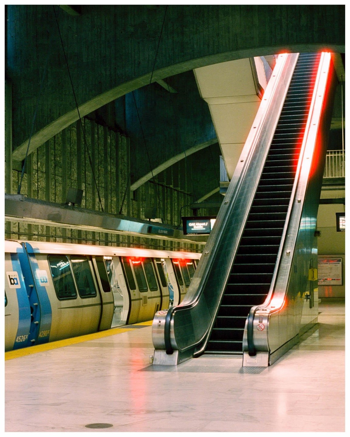 An escalator with red lights on its side stands next to a train at a station.