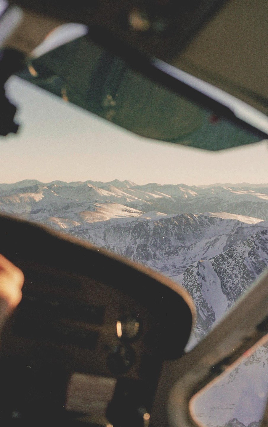 A view from an airplane cockpit shows snow-covered mountains under a clear sky.