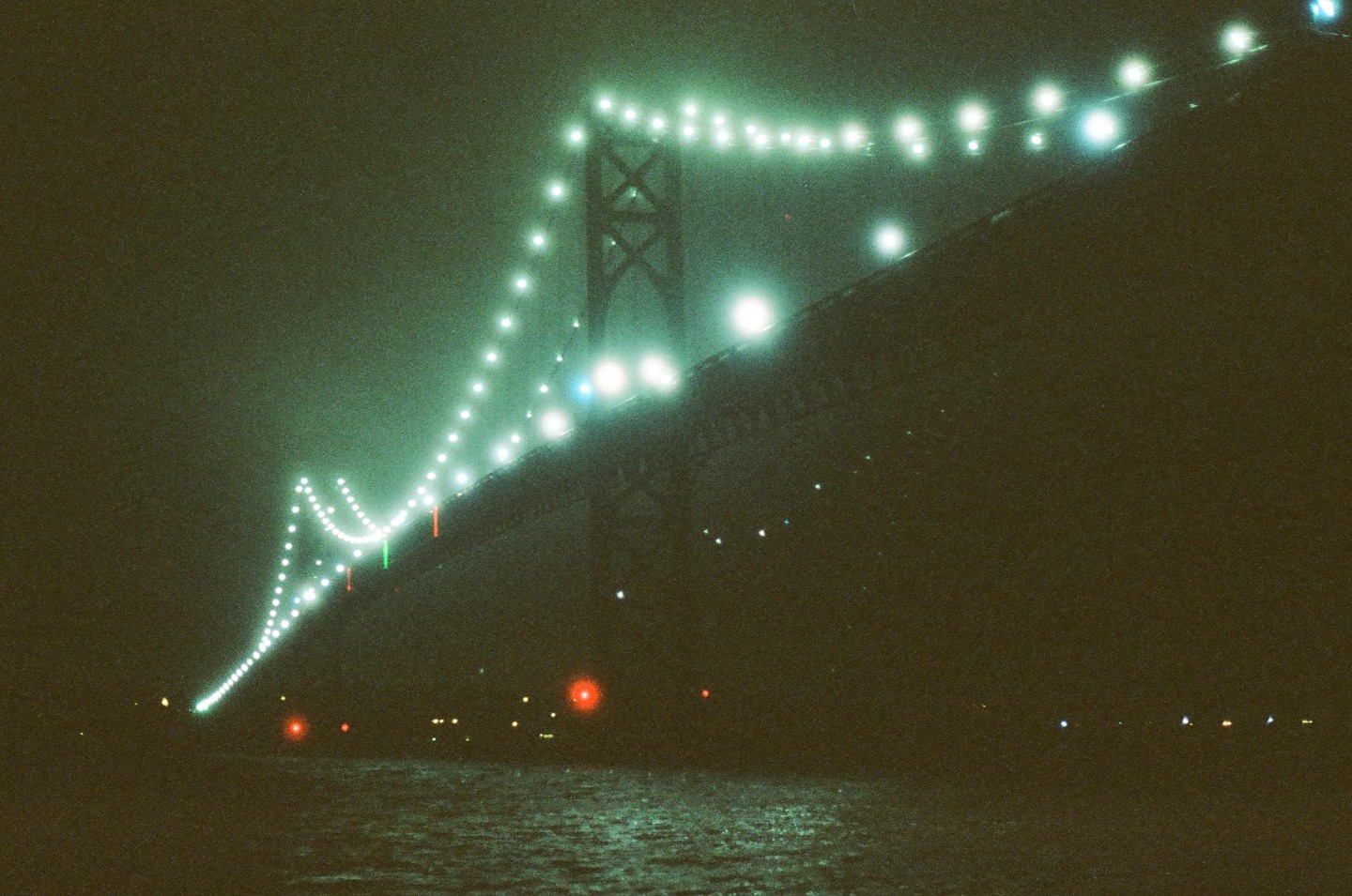 A bridge illuminated with many lights stretches across a body of water at night.