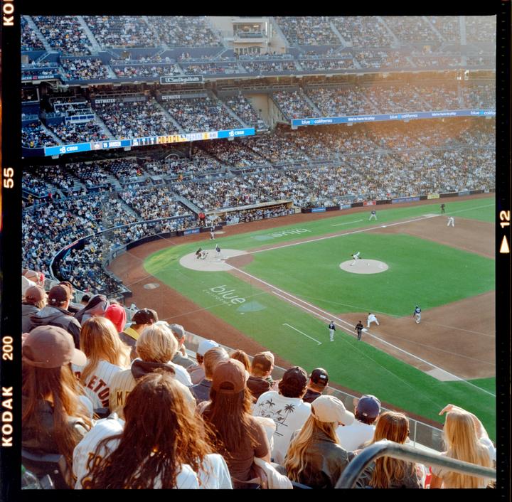 A baseball game is in progress at a stadium filled with spectators, viewed from an elevated perspective behind the crowd.