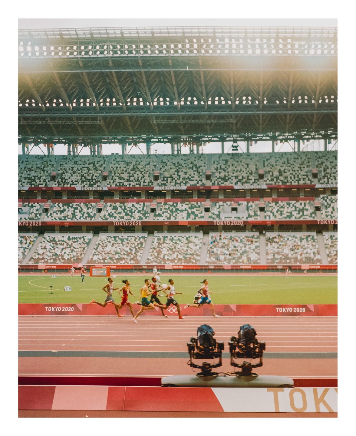 Several men run on a track in a stadium with empty seats.