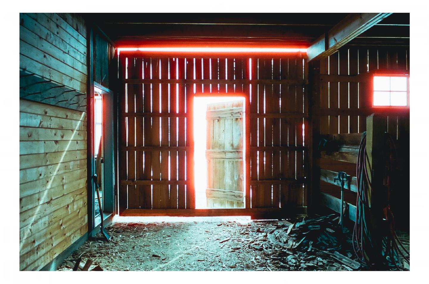 Sunlight streams through the open door and window of a wooden barn, illuminating dust motes in the air.