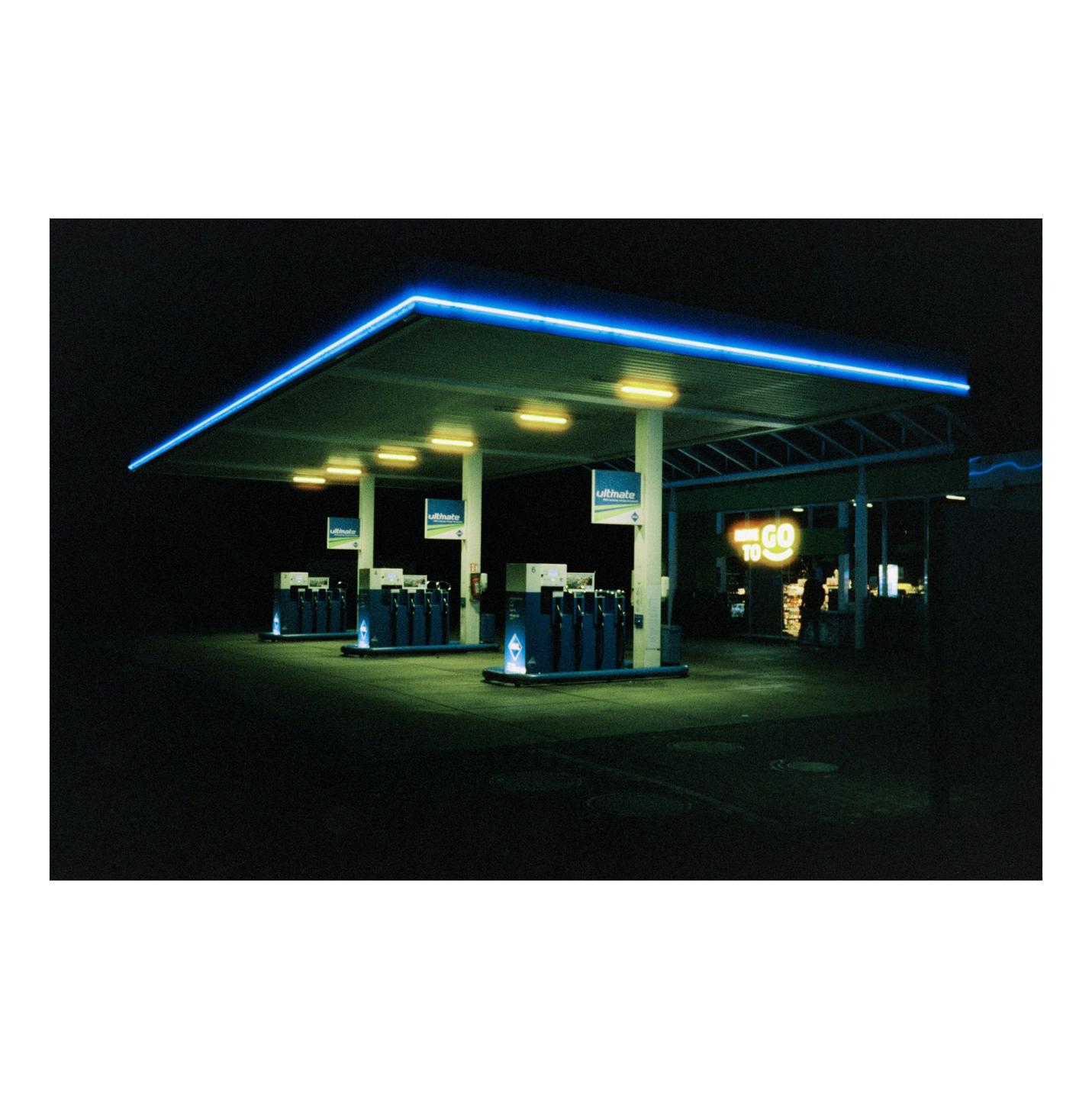 A gas station with blue neon lights and yellow interior lights stands empty at night.