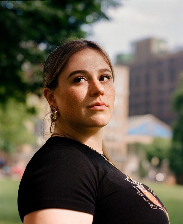 A woman with freckles looks over her shoulder in a sunlit outdoor portrait.