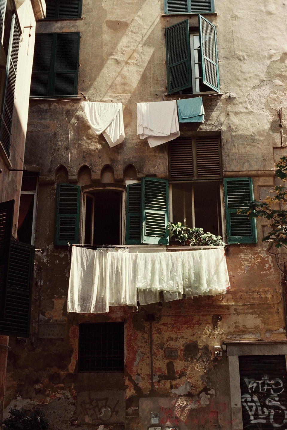 Laundry hangs to dry from clotheslines strung across the facade of an old building with green shutters.