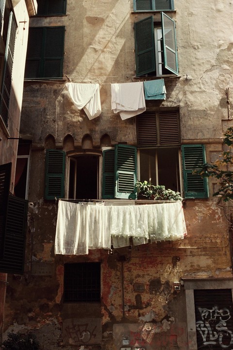 Laundry hangs to dry from clotheslines strung across the facade of an old building with green shutters.