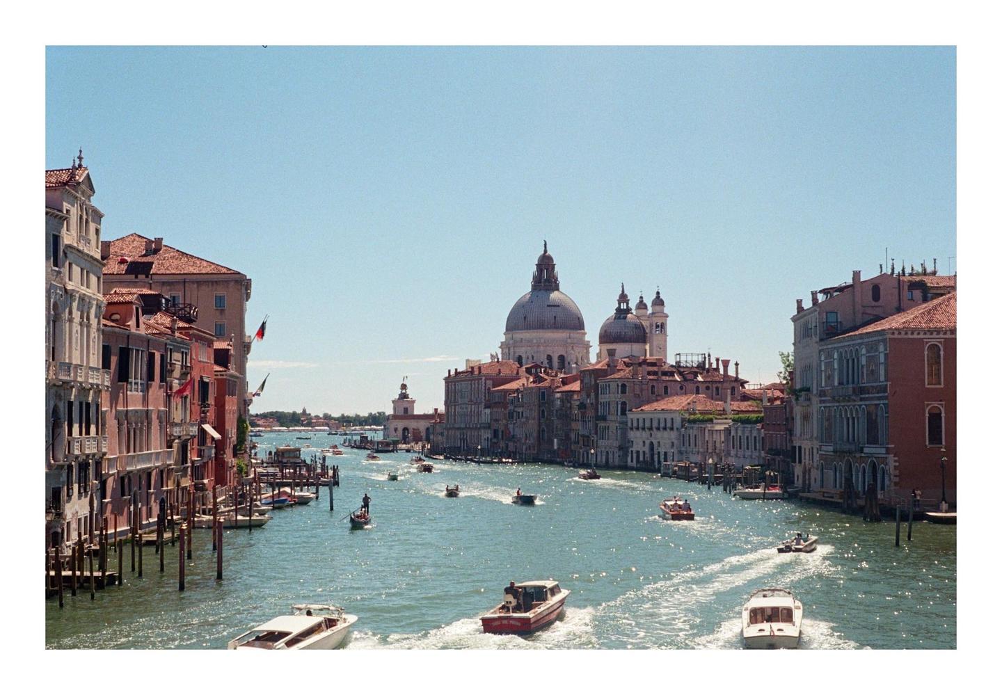 A wide canal with many boats is surrounded by historic buildings under a clear sky.