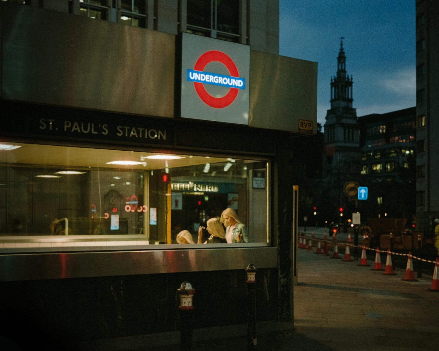 Two women are visible through the window of the St. Paul's Underground station at night.