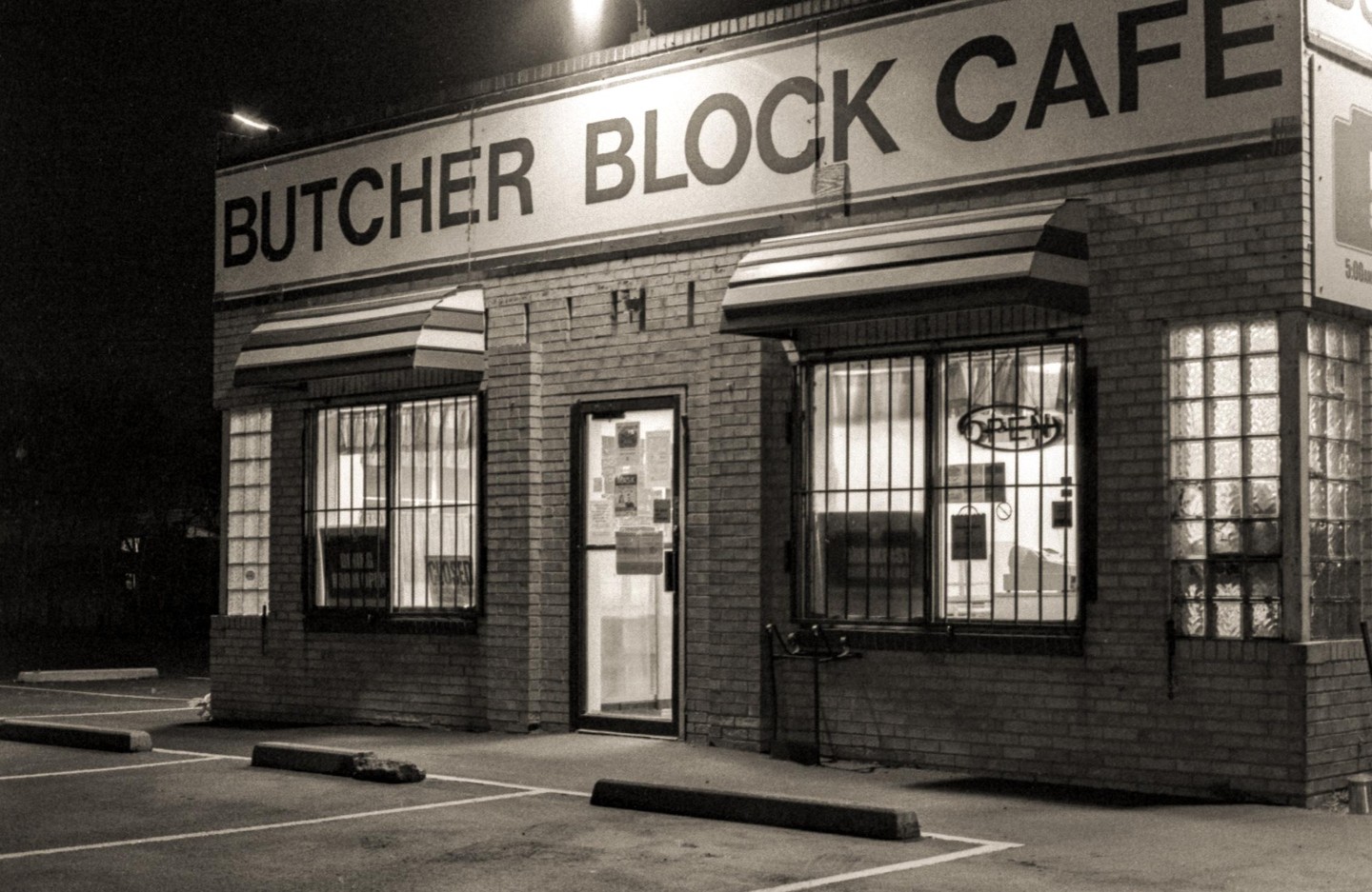 A brick cafe with an "OPEN" sign in the window is illuminated at night.