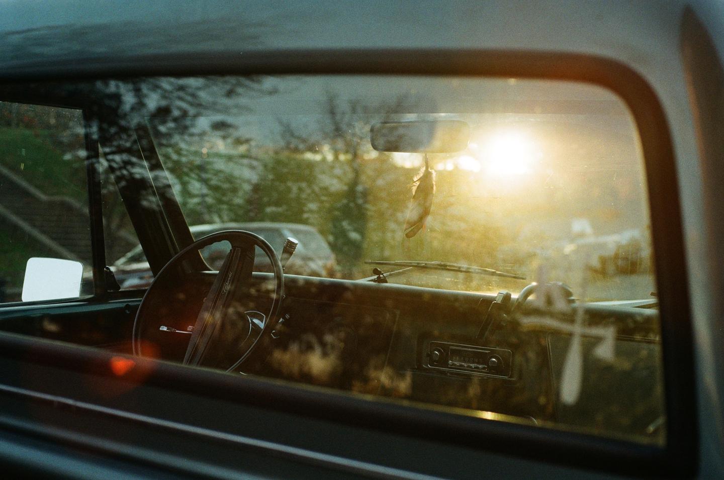 The interior of a classic car is visible through the window, with a bright sun flare in the background.
