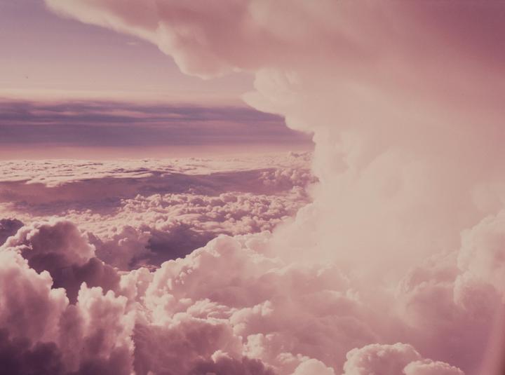 An aerial view shows a vast expanse of clouds under a sky with a purple and pink hue.