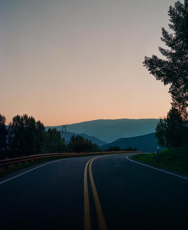 A winding road with a double yellow line leads into a mountain range at dusk.
