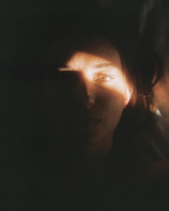 A woman's face is partially illuminated by a strong beam of light in a dark setting.