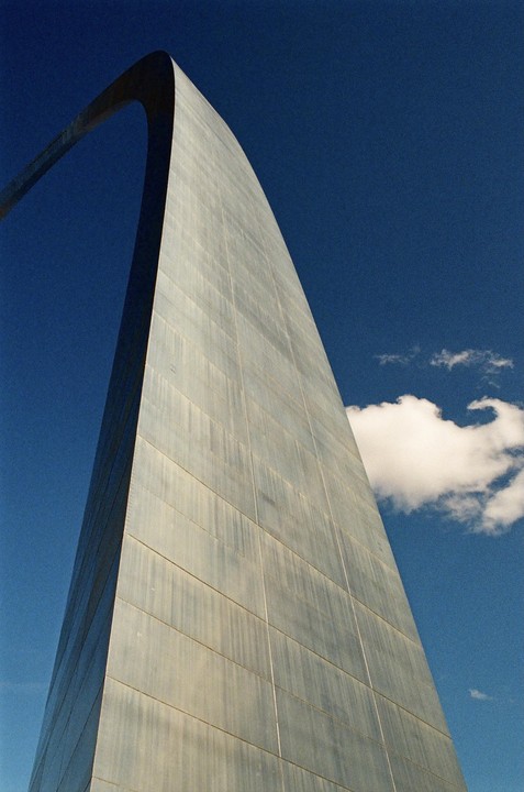 The Gateway Arch rises into a clear blue sky with a single cloud.