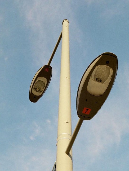 Two streetlights extend from a pole against a blue sky.