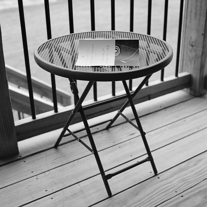 A book titled "Zen in the Art of Archery" rests on a small round metal table on a wooden deck.